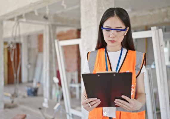Young chinese woman builder reading document at construction site